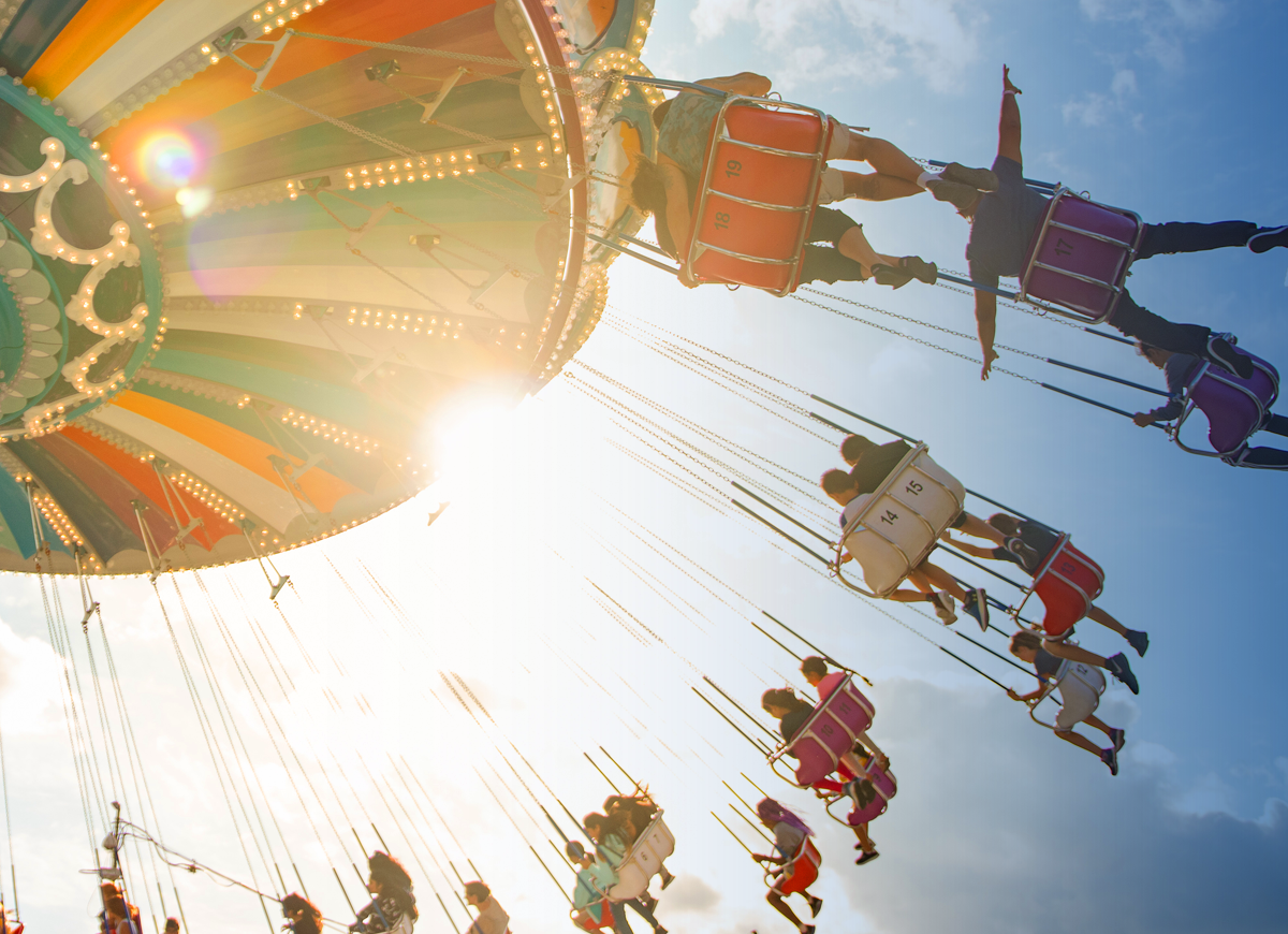 View of riders on a swing carousel ride, looking up from the ground toward the sky